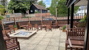 An outdoor patio area with wooden furniture and a fire pit. - The Swan Inn (Newbury)
