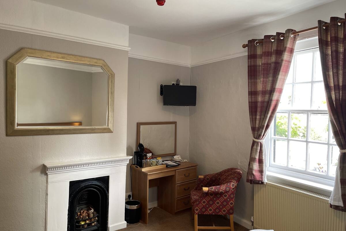 A room with a fireplace, a desk, a chair, a television, and a window with curtains.