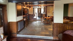 A bar area with wooden bar stools and a counter, a seating area with tables and chairs, and a stone-tiled floor. - The Swan Inn (Newbury)