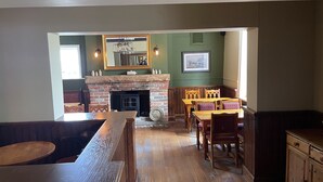 A cozy dining area with a brick fireplace, wooden furniture, and a large mirror above the mantel. - The Swan Inn (Newbury)