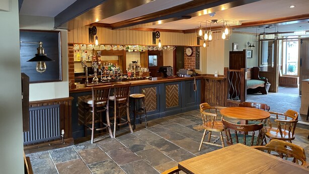 A bar area with a counter, stools, and a round table with chairs. There is a clock on the wall and a window in the background. - The Swan Inn (Newbury)
