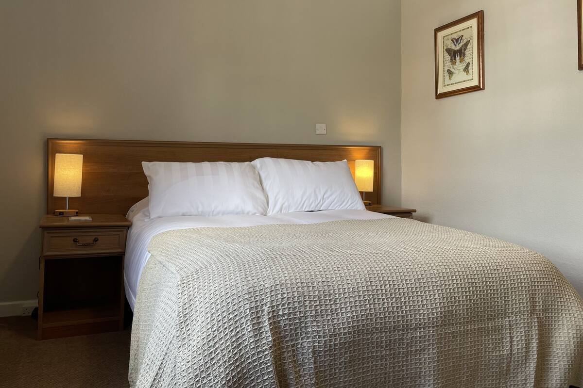 A neatly made bed with white linens and a textured blanket, flanked by wooden nightstands with lamps.