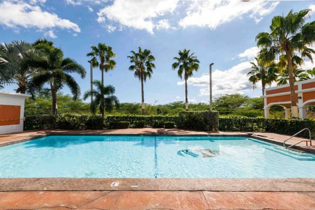 Una piscina con acqua cristallina, circondata da palme e un siepe.