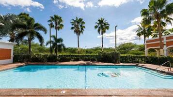 Una piscina con acqua cristallina, circondata da palme e un siepe.