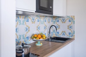 Cozinha com micro-ondas, pia e uma tigela de frutas no balcão.