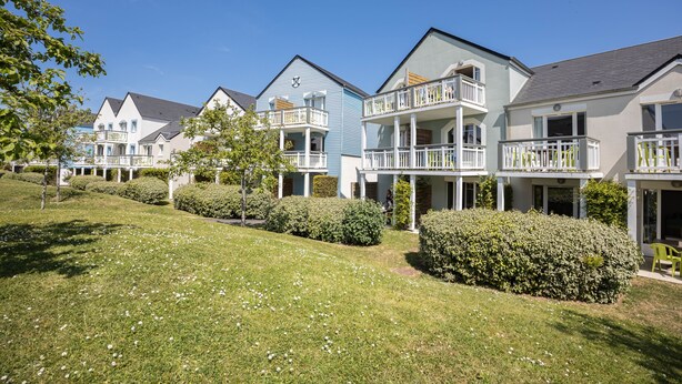 A row of modern, two-story townhouses with balconies, a well-maintained lawn, and a clear blue sky.