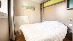 A bedroom with a large bed, a radiator, a window with curtains, and a painting on the wall.