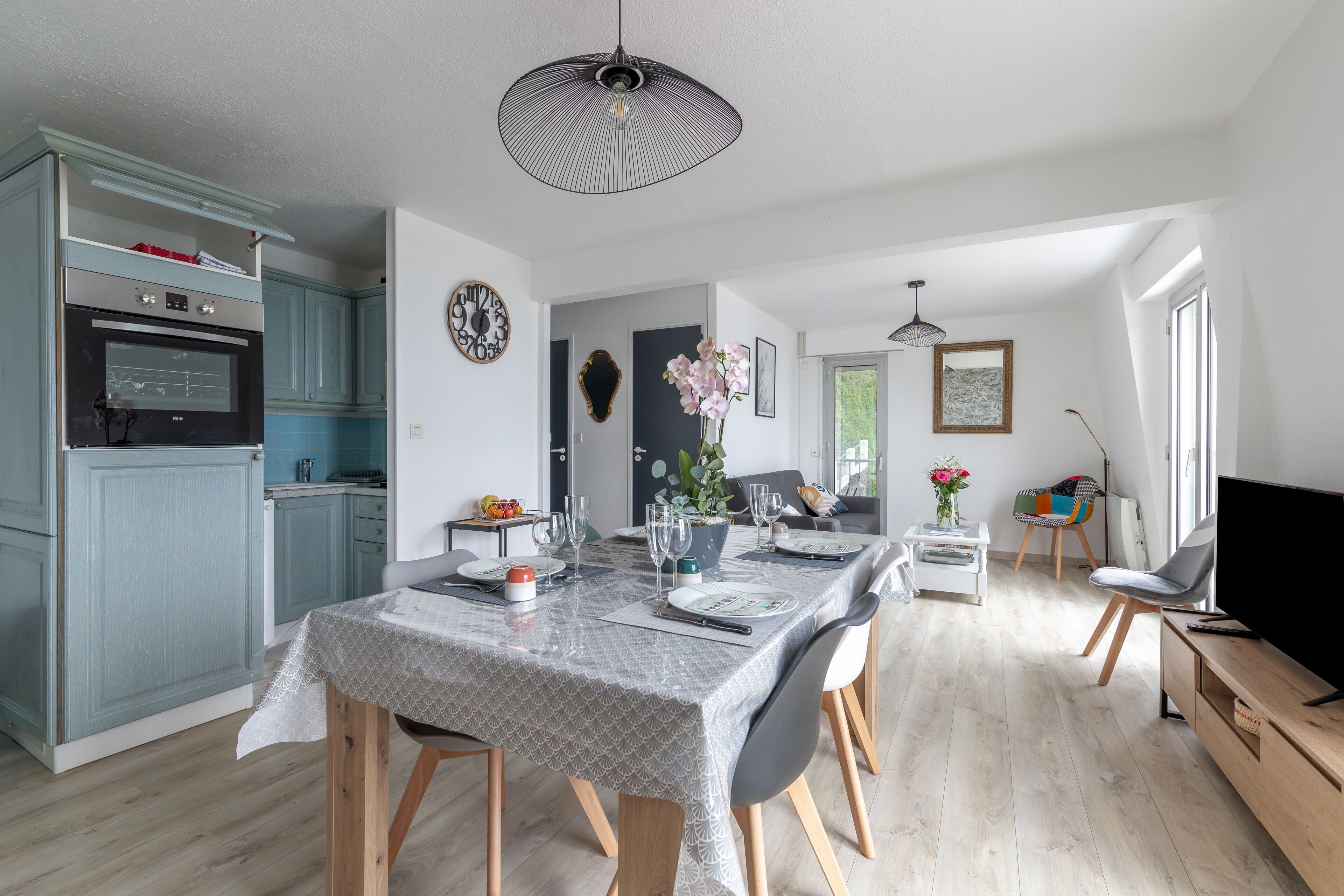 Une cuisine moderne avec des meubles de couleur bleu clair, un four encastré et un coin repas avec une table dressée pour six personnes.