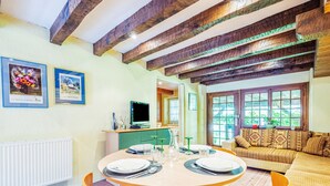 A dining area with a round table set for four, a sofa, and a television in the background. - Surfinia - piscine partagée - proche Europa Park (Hessenheim)