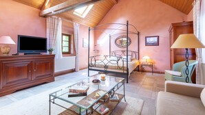 Une chambre confortable avec un lit à baldaquin, une télévision et une table basse en verre sur laquelle sont posés des livres.