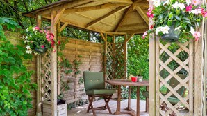 Une pergola en bois, agrémentée d’une table et de chaises, entourée d’une végétation luxuriante.