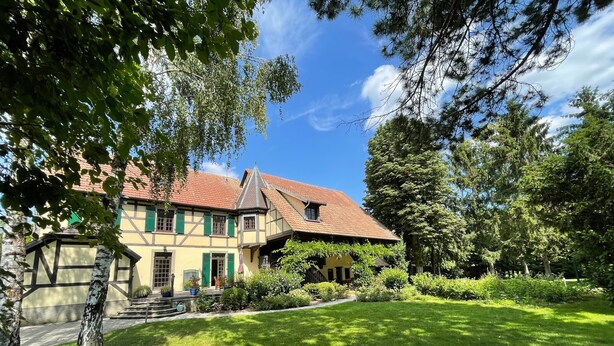Un bâtiment de style européen traditionnel, doté d’un toit en pente, d’une pelouse bien entretenue et entouré d’arbres.