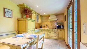 Une cuisine avec des meubles de couleur jaune, une table à manger dressée avec des assiettes et des verres, et une fenêtre donnant sur un paysage verdoyant.