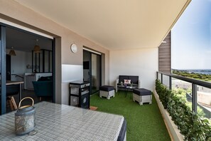 Ein Balkon mit einem grünen Kunstgrasebelag, einem Esstisch mit einem Metallkerzenhalter, Korbmöbeln und Blick aufs Meer.