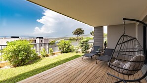 Terraza de madera con una hamaca colgante y una mesa, con vista a una zona cubierta de césped y una cadena montañosa distante.
