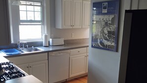 Una cocina con armarios blancos, lavavajillas integrado, estufa y ventana.