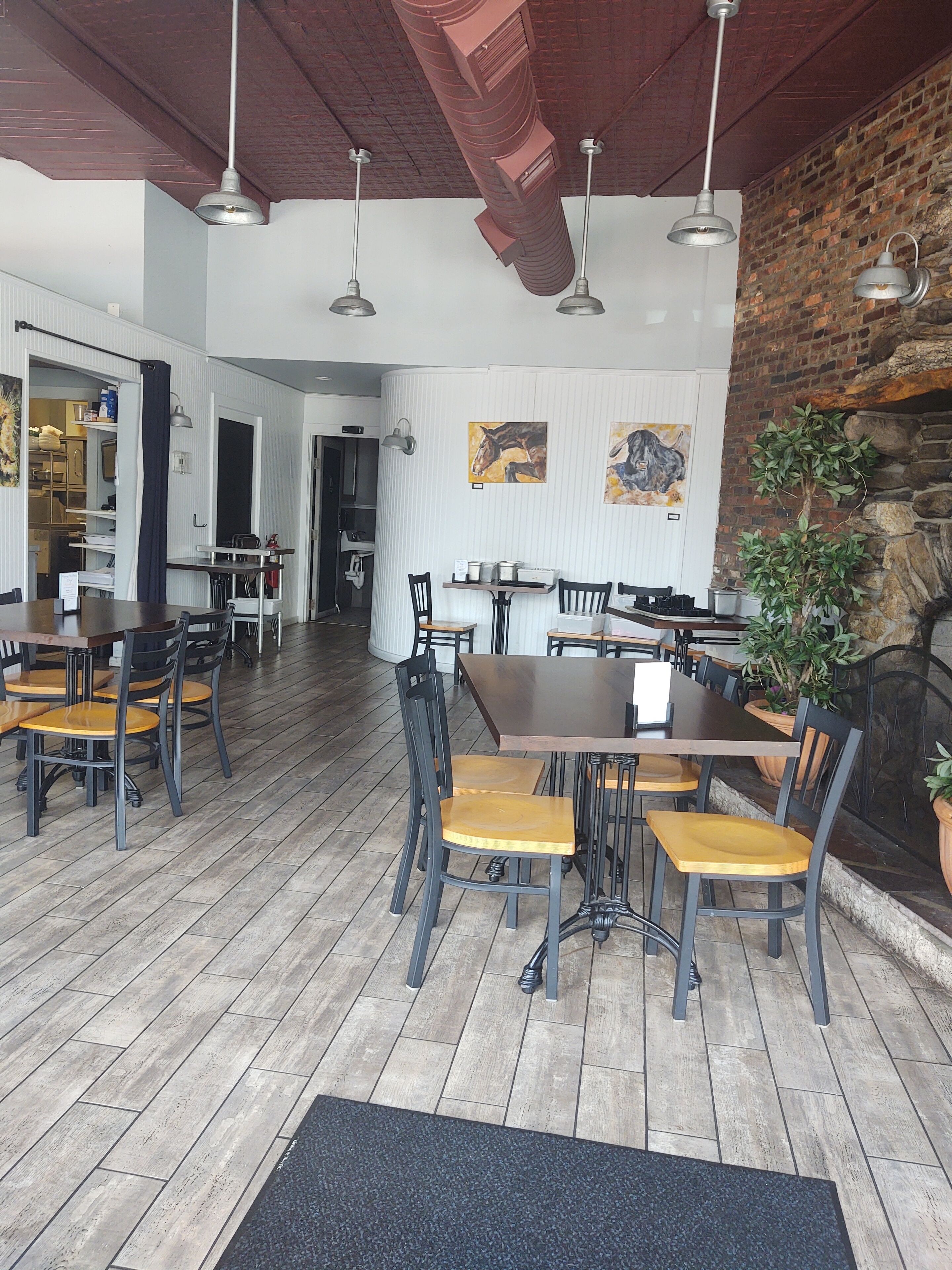 Ein Restaurant mit Holzboden, schwarzen und hölzernen Stühlen und hängenden Pendelleuchten.