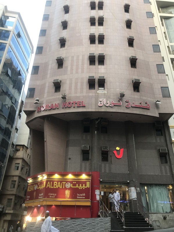 Un hotel con un letrero visible que dice "NORAN HOTEL" y un restaurante cercano llamado AlBait AlBait Shawarma.