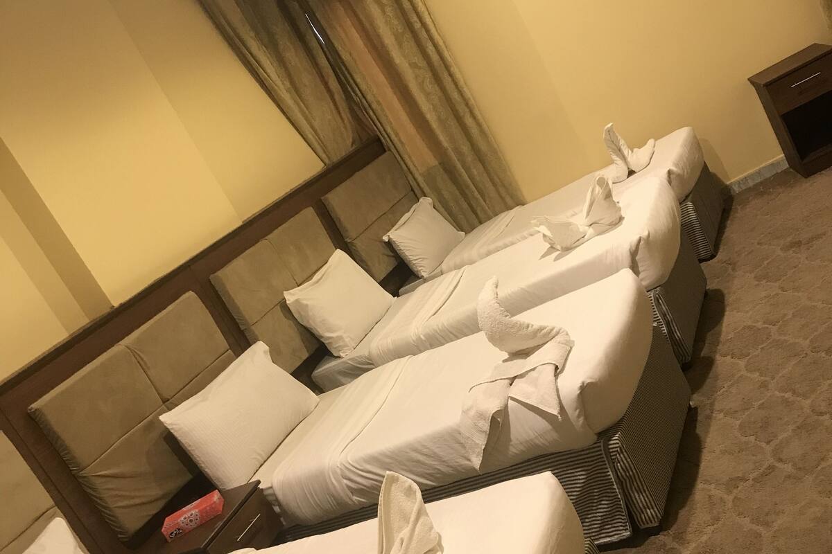 Hotellihuone, jossa on kaksi sänkyä, puinen pääty, yöpöytä ja matolla peitetty lattia.