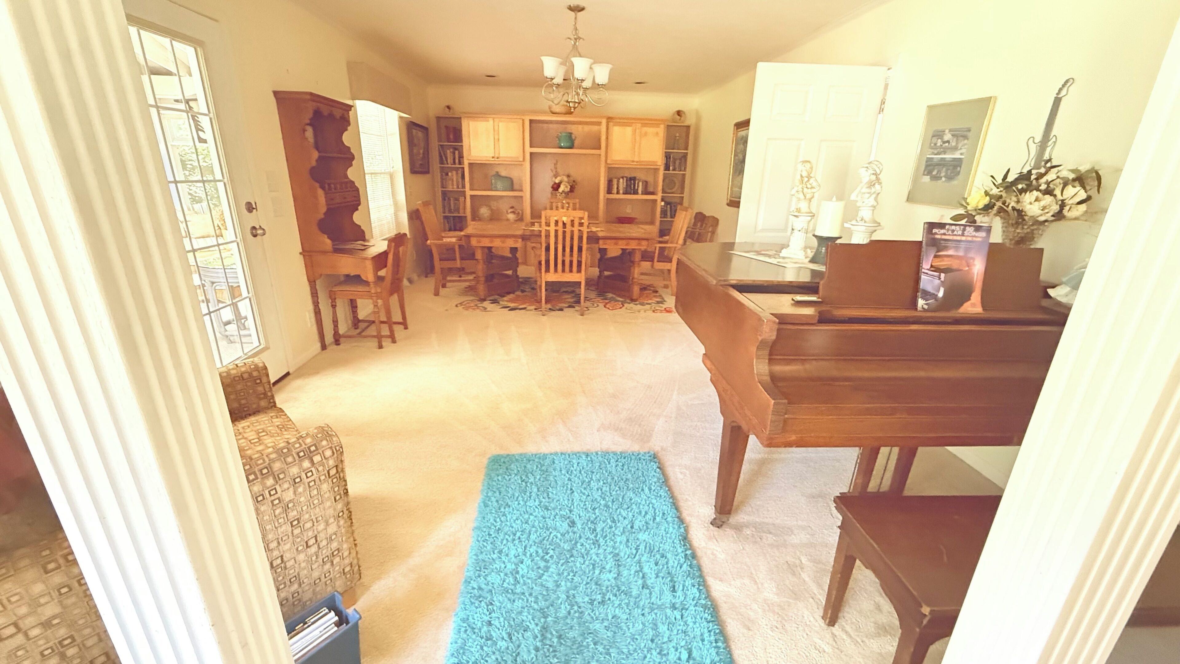 A spacious living room with a dining area, a piano, and a bookshelf.