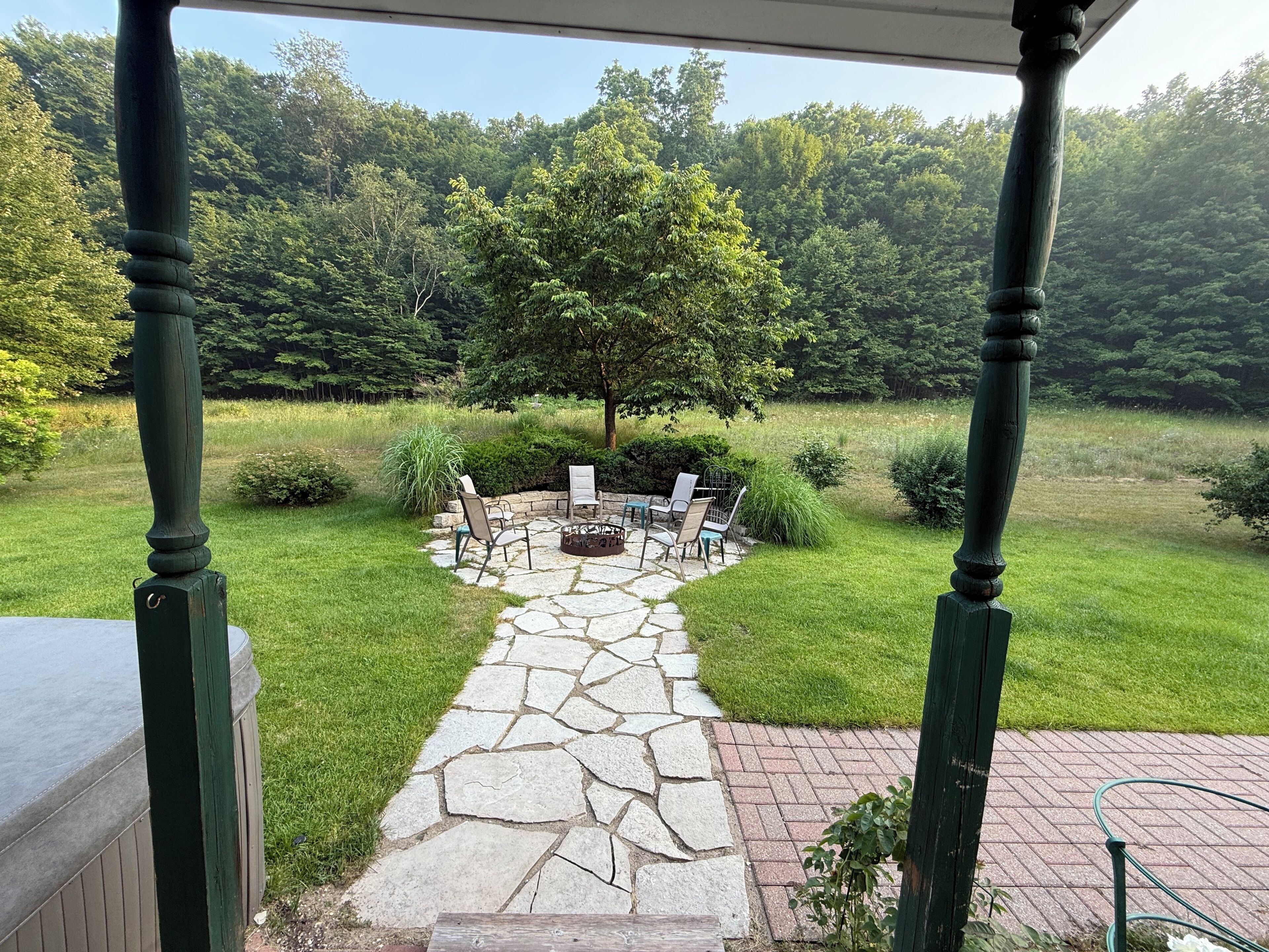 A stone pathway leading to a fire pit with chairs, surrounded by a grassy area and trees.
