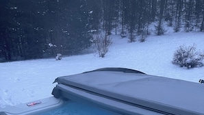 Uma banheira de hidromassagem com capa azul, rodeada por neve e árvores.