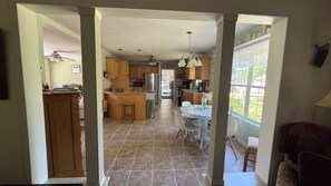 A spacious kitchen with a central island, a dining area with a white table, and a view through a window.