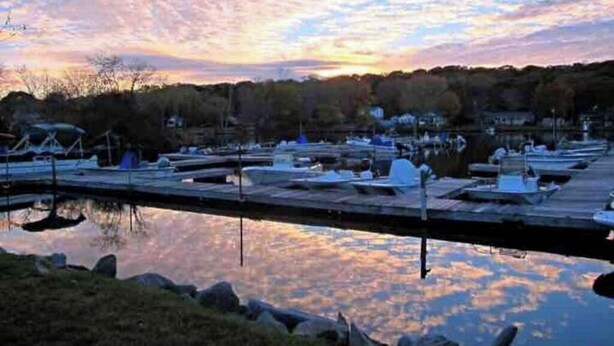 Un port de plaisance avec des bateaux amarrés, une eau calme et un ciel au coucher du soleil.