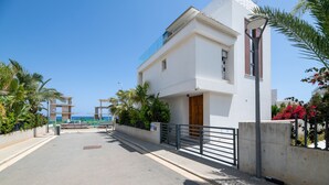 A modern two-story building with a balcony, a gated entrance, and a clear view of the sea.