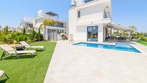 A modern two-story house with a swimming pool, outdoor seating, and a well-maintained lawn.