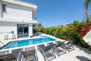 A modern building with a swimming pool, outdoor seating, and lush greenery.
