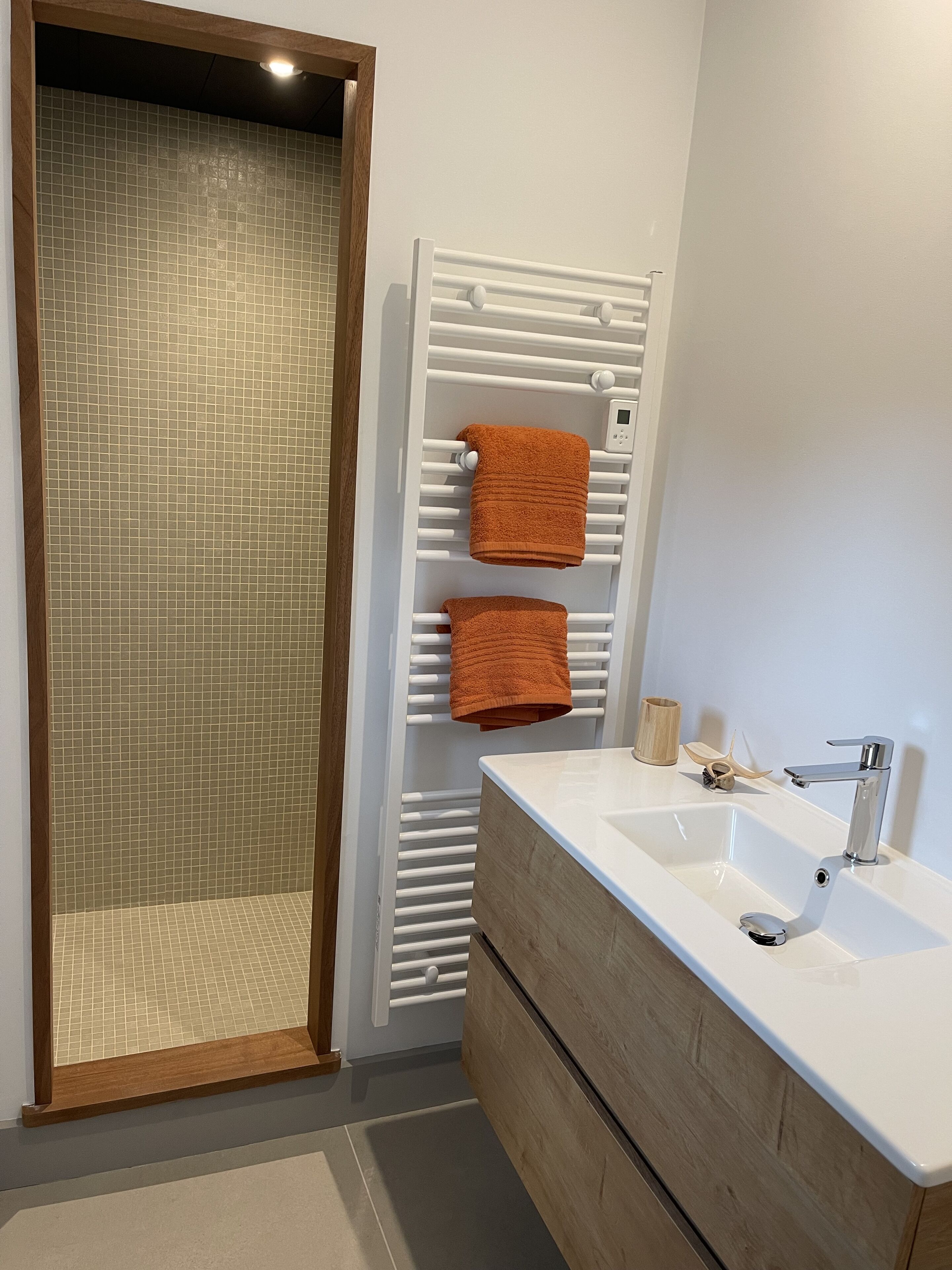 Une salle de bain moderne avec un grand miroir, un lavabo blanc et un porte-serviettes avec deux serviettes.