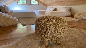 Un dormitorio acogedor en el ático, con techo inclinado, vigas de madera, dos camas, alfombras mullidas y un otomano decorativo.