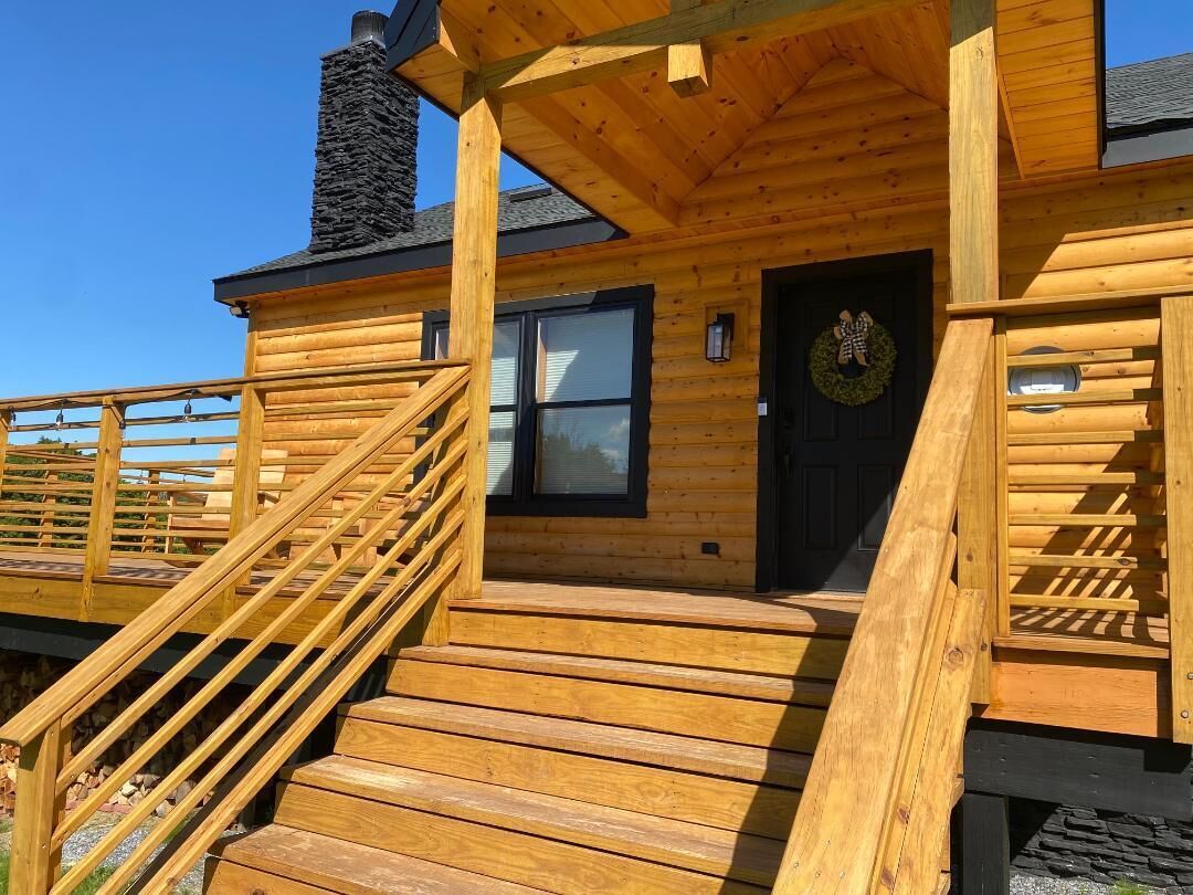 A wooden cabin with a wooden staircase leading to a front door, a window, and a chimney.