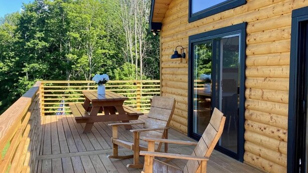 Una terraza de madera con mobiliario exterior y un vidrio que da a una habitación.