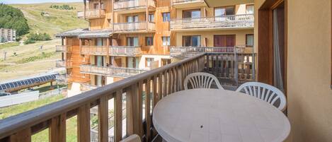 A balcony with a round table and chairs, overlooking a mountainous area with multiple wooden buildings.
