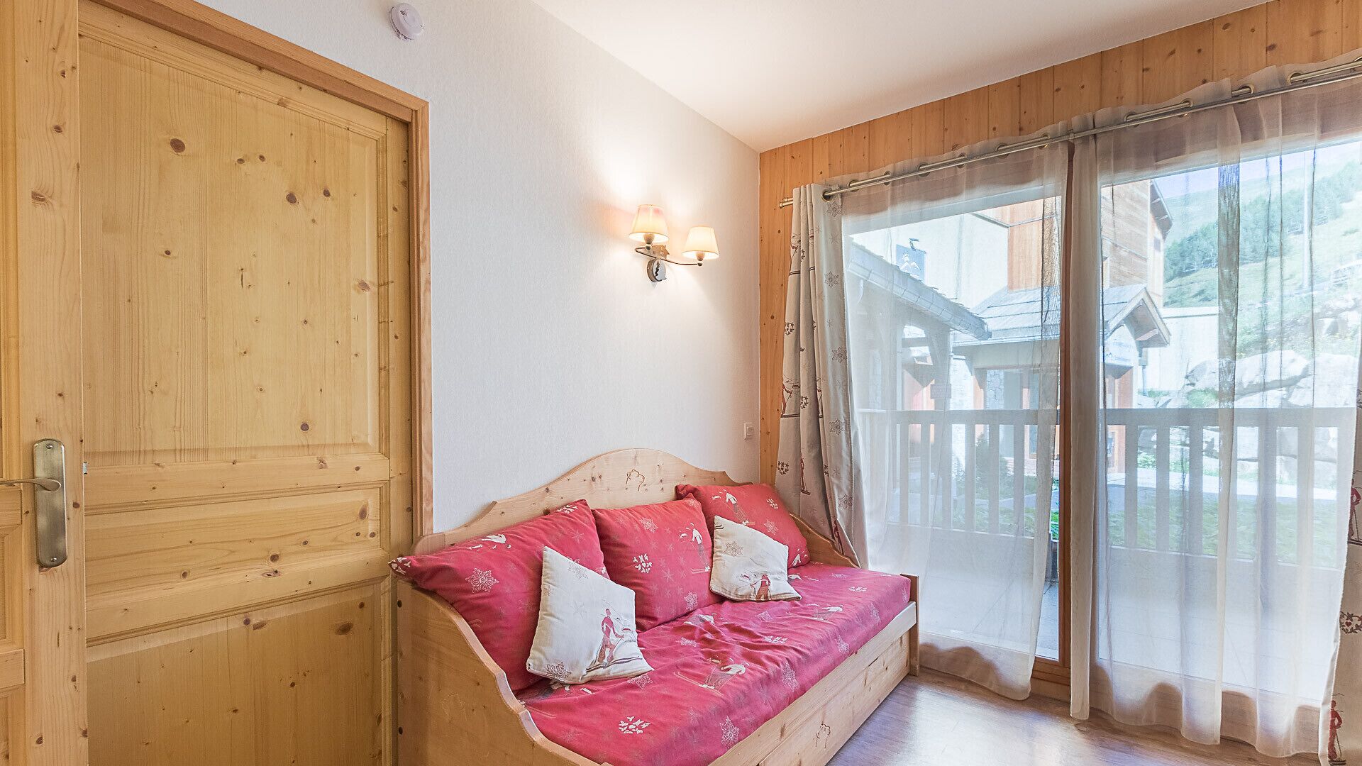 A wooden room with a bed, a wooden door, and a window with curtains.
