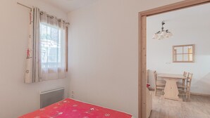 A room with a bed, a window with curtains, a radiator, a table with chairs, and a wooden door. - Bright apt 4 ppl near the ski runs, balcony (Orcières)