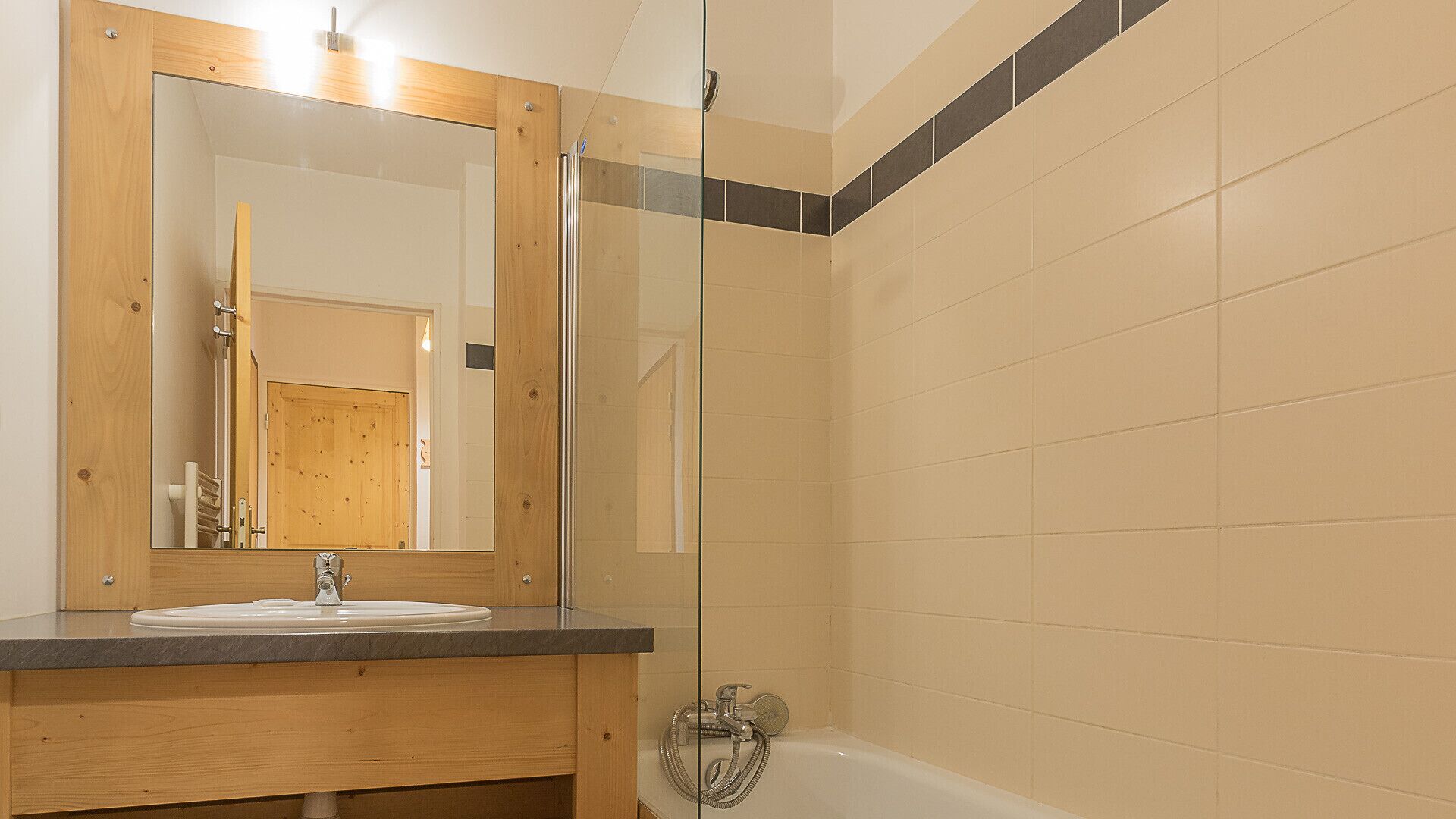 A bathroom with a wooden vanity, a sink, a mirror, and a shower area.