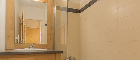 A bathroom with a wooden vanity, a sink, a mirror, and a shower area.