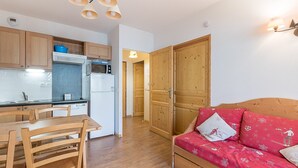 A compact kitchen with wooden cabinets, a microwave, and a refrigerator. There is a dining table with chairs and a red sofa with decorative pillows. - Bright apt 4 ppl near the ski runs, balcony (Orcières)
