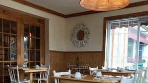A dining area with wooden tables and white chairs, a large rug, and a decorative wall piece. - auberge maison gagne (Tadoussac)