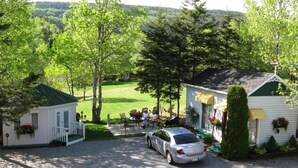 A small lodge with a gravel driveway, a car parked in front, and a dining area with outdoor seating. - auberge maison gagne (Tadoussac)