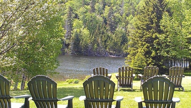 A lakeside view with several Adirondack chairs facing the water. - auberge maison gagne (Tadoussac)