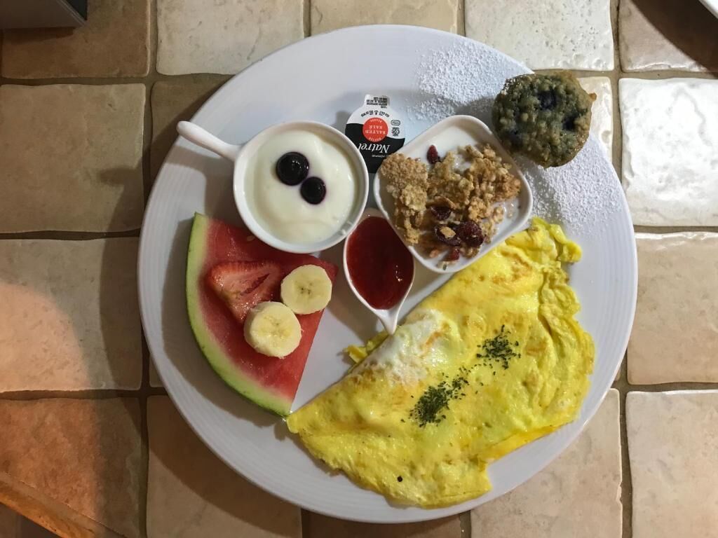 A plate with an omelette, watermelon slices, bananas, yogurt with berries, granola, and a drink.