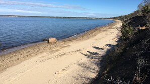 A beach with clear blue water, a sandy shore, and a distant shoreline with buildings. - Newly renovated Modern East Hampton Home / September available (East Hampton)
