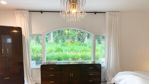 A bedroom with a large window, a dark wooden dresser, a bed, and a chandelier. - Newly renovated Modern East Hampton Home / September available (East Hampton)