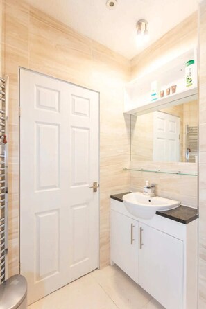 A bathroom with a white door, a glass shower enclosure, a white sink with a black countertop, and a mirror above the sink.