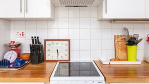 Moderni keittiö, jossa on valkoiset kaapit, sisäänrakennettu liesi ja seinällä oleva kello.