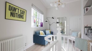 Ein helles Wohnzimmer mit einem blauen Sofa, einer weißen Treppe und einem Schild mit der Aufschrift 'DON'T SAY NOTHING'.